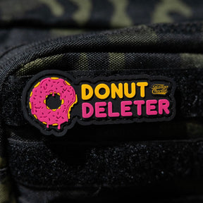 The Donut Deleter - Patch by Tango Charlie Apparel is a 3-inch 3D PVC patch with a pink sprinkled donut and “DONUT DELETER” in yellow/pink, plus a small Giant Mouse logo. It attaches to fabric surfaces with Velcro backing.