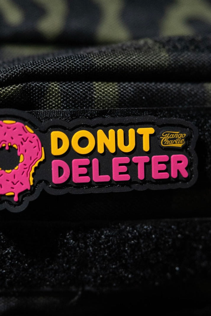 The Donut Deleter - Patch by Tango Charlie Apparel is a 3-inch 3D PVC patch with a pink sprinkled donut and “DONUT DELETER” in yellow/pink, plus a small Giant Mouse logo. It attaches to fabric surfaces with Velcro backing.