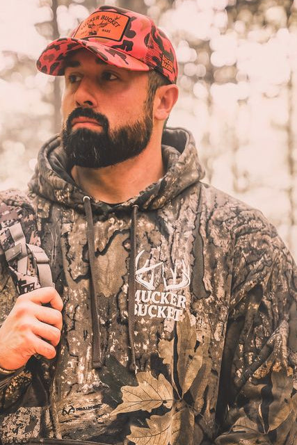 A bearded man wearing The Rut Realtree Premium Hoodie and a matching camouflage baseball cap.