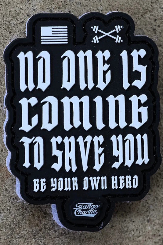 The No One Is Coming To Save You PVC Patch by Tango Charlie Apparel features white gothic text, a small flag, and crossed barbells above the message. The patch displays the Tango Charlie logo at the bottom and is shown on a stone surface.