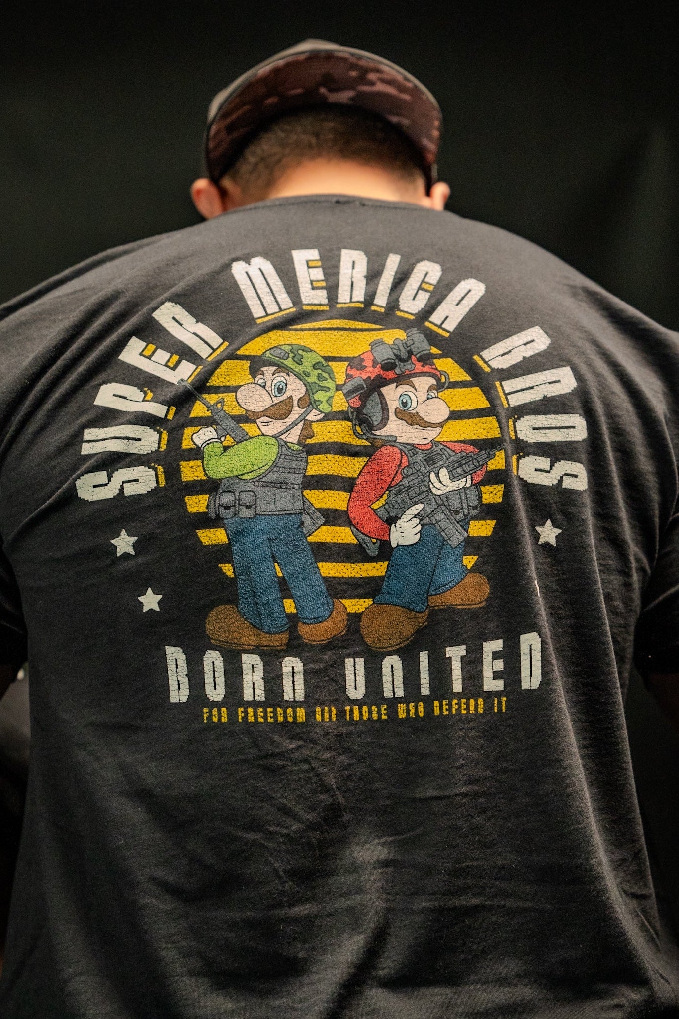 A man wears a Born United Private Label tee featuring a vivid graphic of two cartoon-like plumbers. Super Merica Bros and Born United are on the back, adding an all-American flair to your wardrobe.