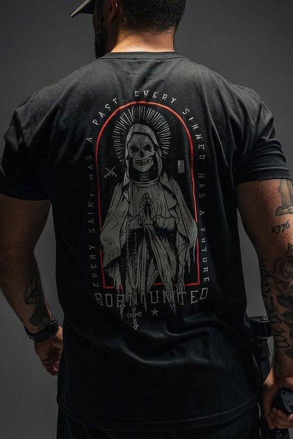 A man wears the Saints and Sinners OG Tee by Born United Private Label, a black shirt featuring a skeletal figure in prayer with the text EVERY SAINT HAS A PAST, EVERY SINNER HAS A FUTURE, and BORN UNLUCKY—bold and inspiring.