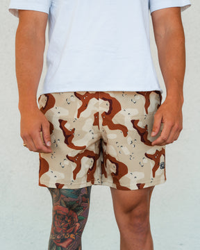 A person wearing a white T-shirt and Tango Charlie Apparel Men's Performance Training Shorts | 5.5"- Choco Chip stands against a light background, their tattooed leg adding flair to these versatile training shorts.