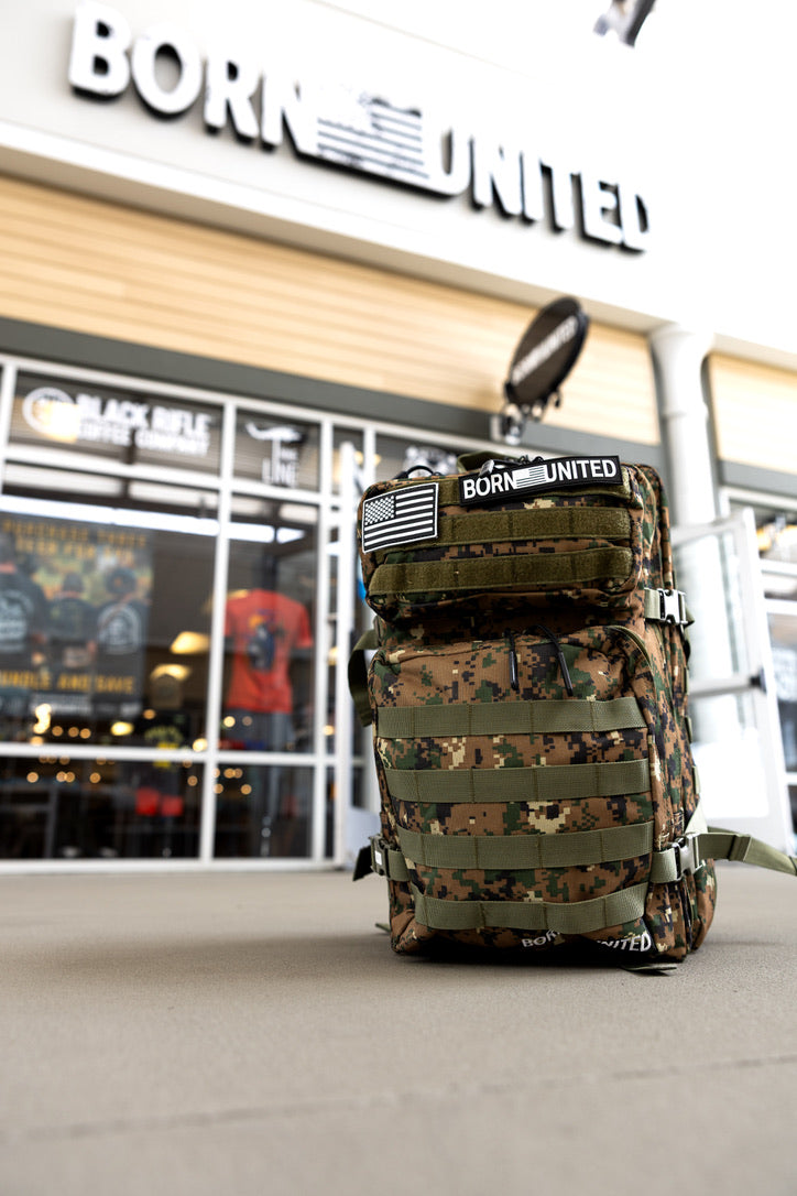The Digi-Cam Tac-Pac - 45L tactical backpack by Born United Private Label, with BORN UNITED and American flag patches, sits outside the store while the Born United Private Label shop sign appears in the background.