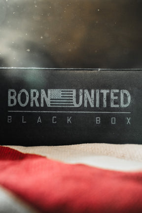 The Born United Private Label’s "Born United Black Box - Tactigator" features an American flag-themed black box with "BLACK BOX" beneath, plus a folded flag in front—ideal for fans of limited edition or mystery tees.