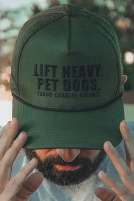 Someone wearing the Lift Heavy, Pet Dogs Snapback- Green by Tango Charlie Apparel, a sweat-resistant dog lover hat with "LIFT HEAVY. PET DOGS." on the front, has their face partially covered and hands raised.