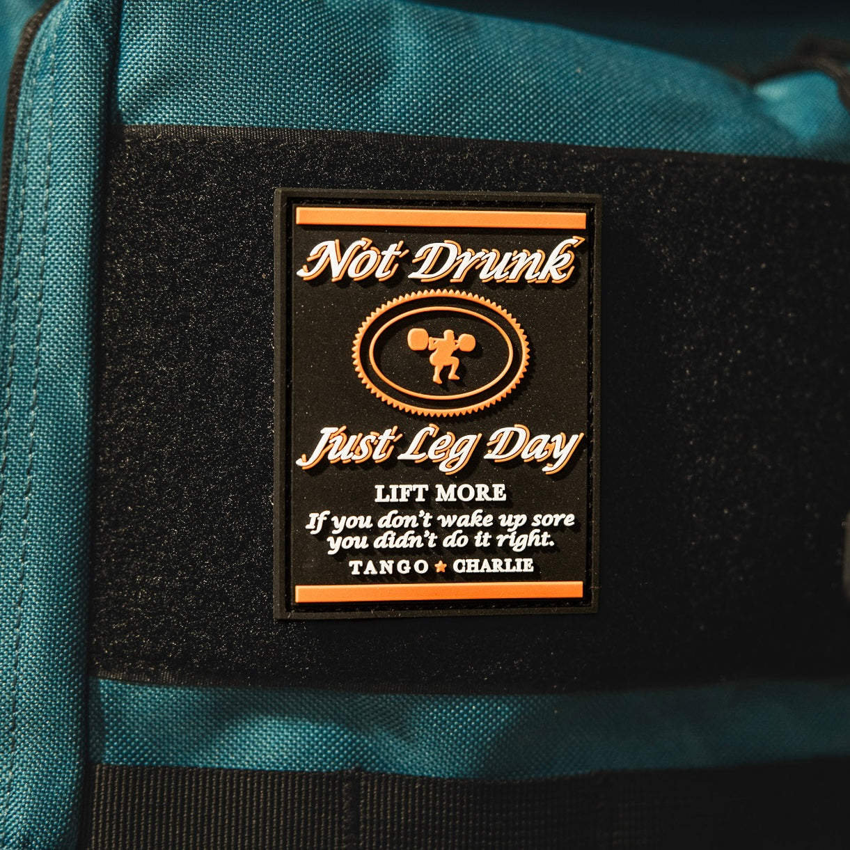A 3-inch Velcro patch by Tango Charlie Apparel reads "Not Drunk, Just Leg Day. LIFT MORE. If you don’t wake up sore you didn’t do it right." with a weightlifter silhouette. Product: Not Drunk, Just Leg Day - Patch.