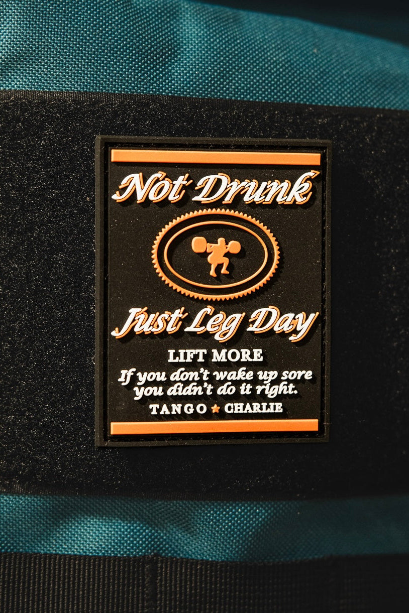 A 3-inch Velcro patch by Tango Charlie Apparel reads "Not Drunk, Just Leg Day. LIFT MORE. If you don’t wake up sore you didn’t do it right." with a weightlifter silhouette. Product: Not Drunk, Just Leg Day - Patch.