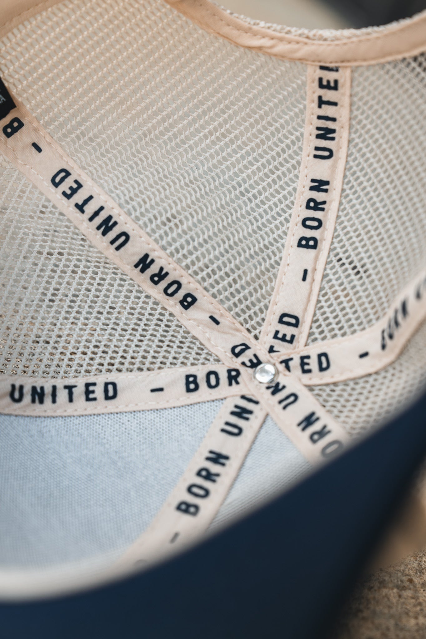 Close-up of the inside of the ’Merica Trucker Snapback by Born United Private Label, featuring breathable mesh and beige straps printed with “BORN UNITED” in black, intersecting at the center with a metal rivet.