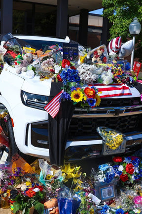 A white SUV adorned with flowers, flags, and tributes stands as a Knight Watch memorial by Born United Private Label. Surrounding gifts from Chesterfield County Police and others honor the fallen hero.