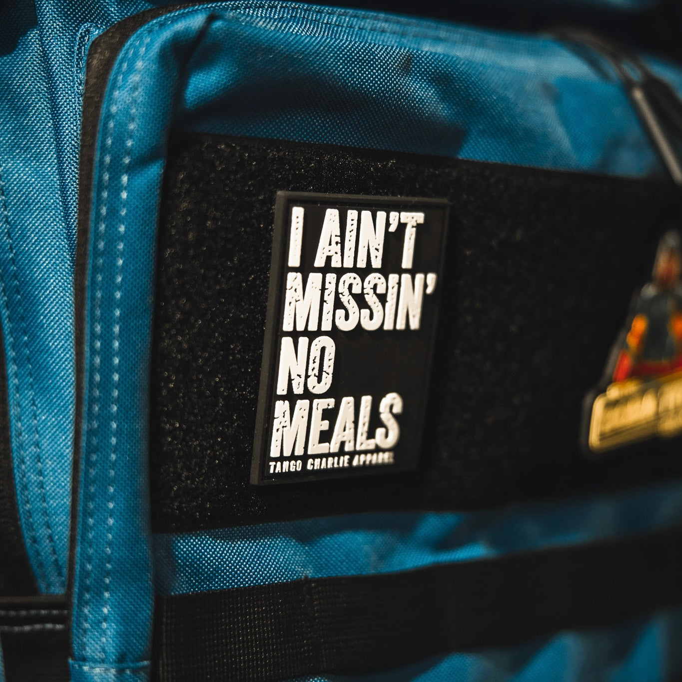 A close-up of the I Ain’t Missin’ No Meals patch by Tango Charlie Apparel, a blue 3D PVC Velcro accessory.