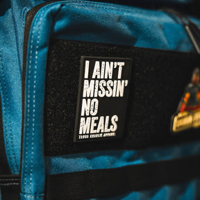A close-up of the I Ain’t Missin’ No Meals patch by Tango Charlie Apparel, a blue 3D PVC Velcro accessory.