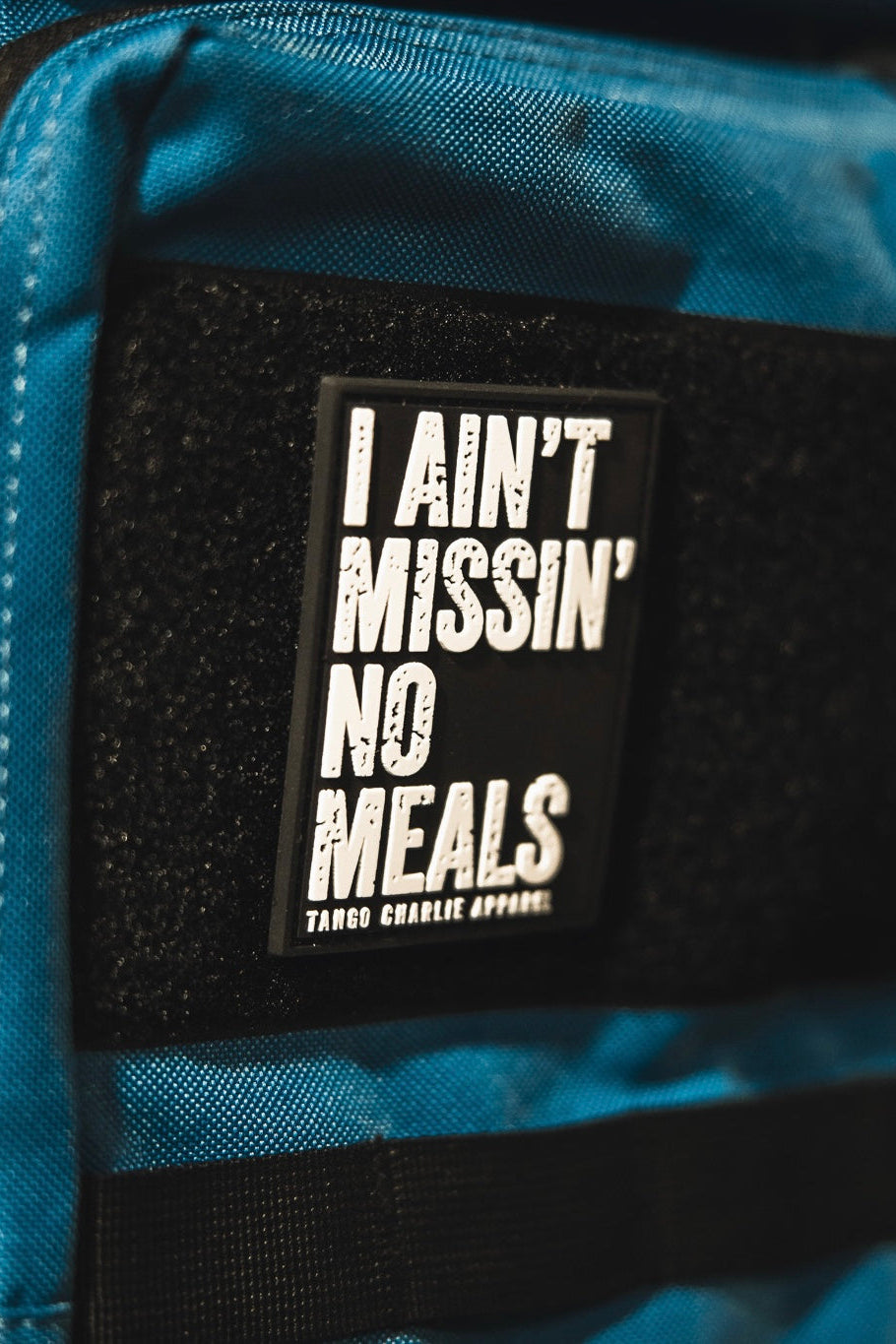 A close-up of the I Ain’t Missin’ No Meals patch by Tango Charlie Apparel, a blue 3D PVC Velcro accessory.