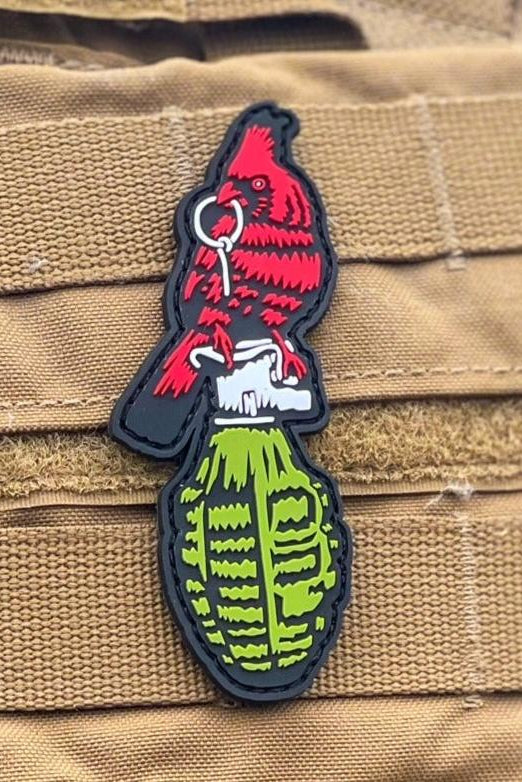 The Beauty and Chaos PVC Patch by Tango Charlie Apparel shows a red cardinal pulling the pin from a green grenade, attached to tan tactical gear with hook-and-loop backing.