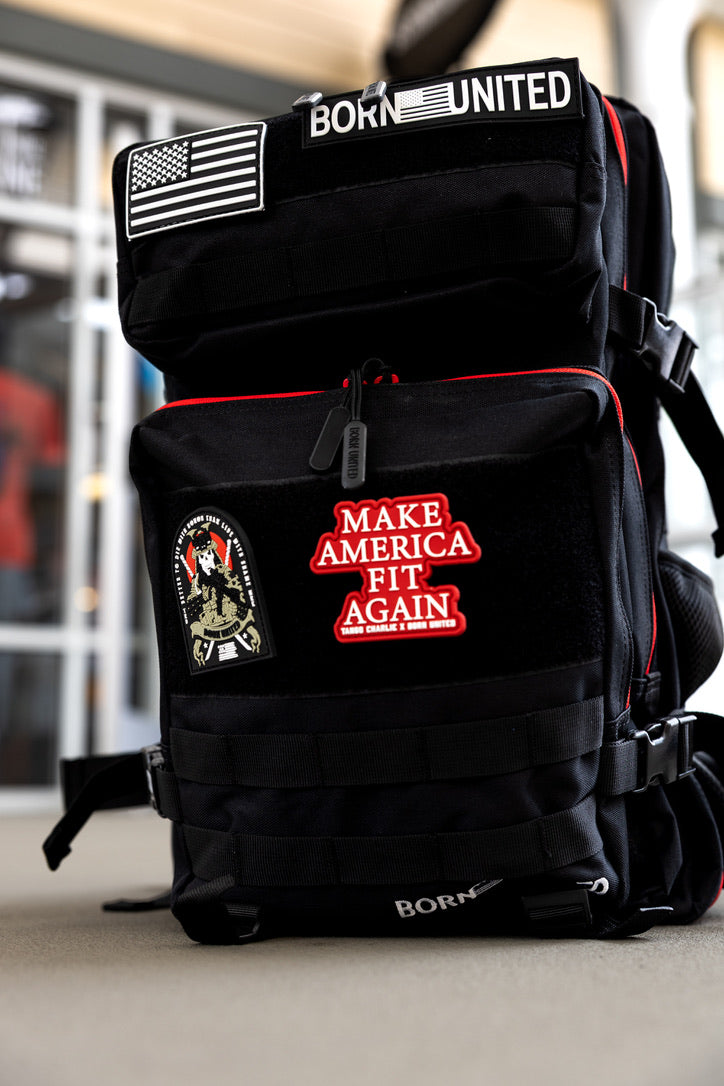 The Black Premium Widow Tac-Pac - 45L by Born United Private Label features MOLLE webbing and patches—American flag, BORN UNITED, MAKE AMERICA FIT AGAIN, and a military-style emblem—and sits on the floor indoors.