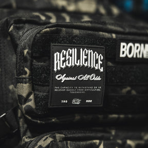 A close-up of the Tango Charlie Apparel "Resilience - Patch," a 3D PVC patch on a camo bag, featuring the phrase "RESILIENCE Against All Odds" to symbolize toughness and overcoming challenges.