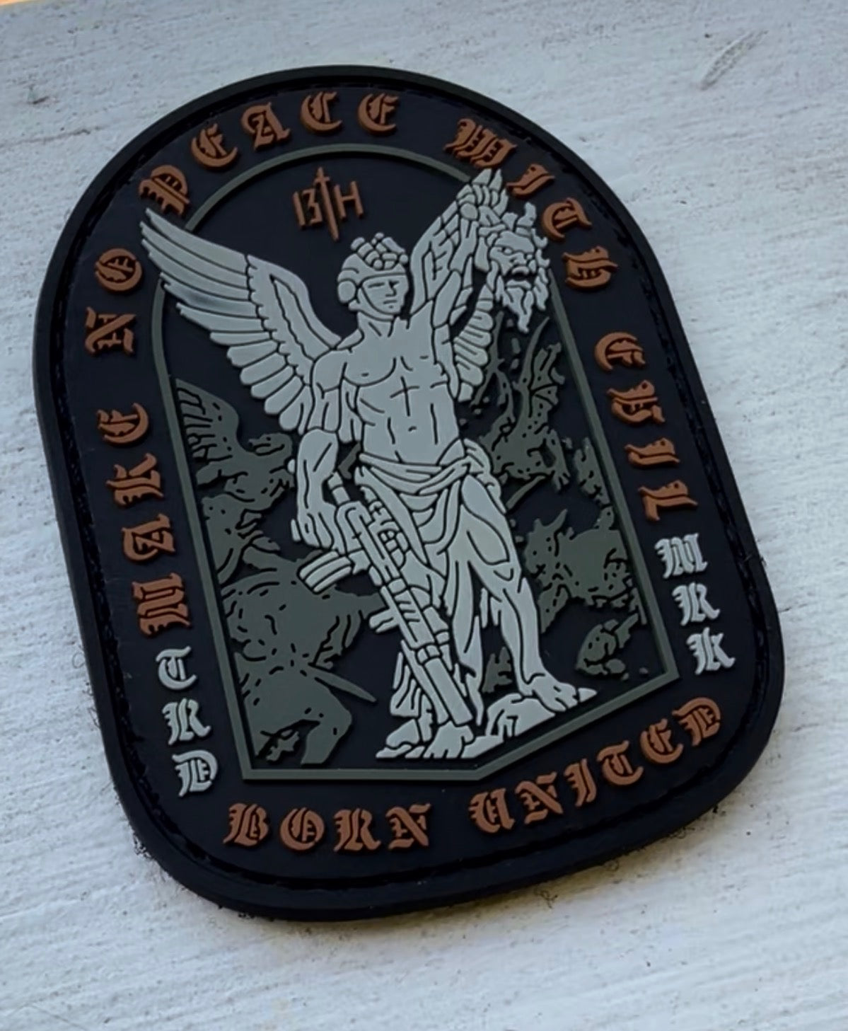 The Make No Peace PVC Patch by Born United Private Label features an angel with a sword and severed head, plus inscriptions "MAKE NO PEACE WITH EVIL," "BORN UNITED," and "TIRDJ MRK 13TH"—ideal for custom patch collectors.