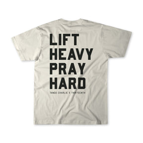 A light gray Lift Heavy. Pray Hard. - Tee from Tango Charlie Apparel, shown from the back with bold black text LIFT HEAVY PRAY HARD and smaller TANGO CHARLIE X THIRTEENTH below, reflecting spiritual resilience.