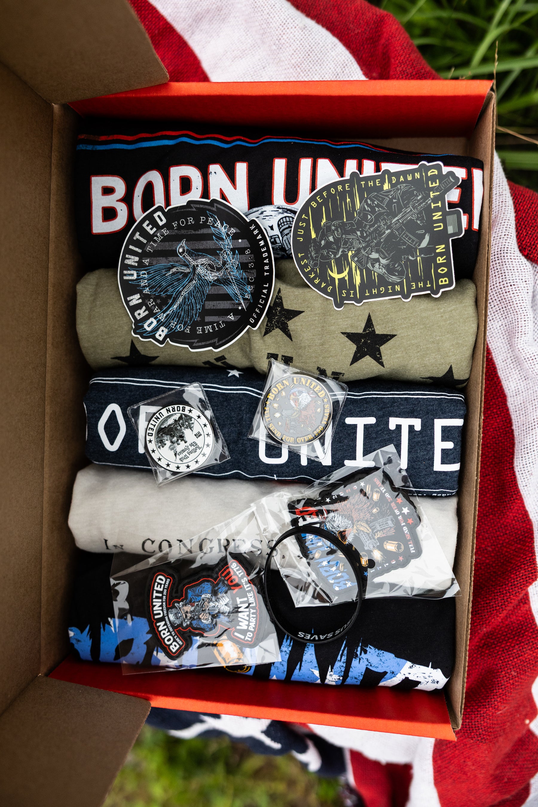 The Born United Private Label Born United Patriot Box, featuring limited edition tees, stickers, and patriotic patches, is perfect for celebrating America's 250th birthday—proudly displayed on an American flag.