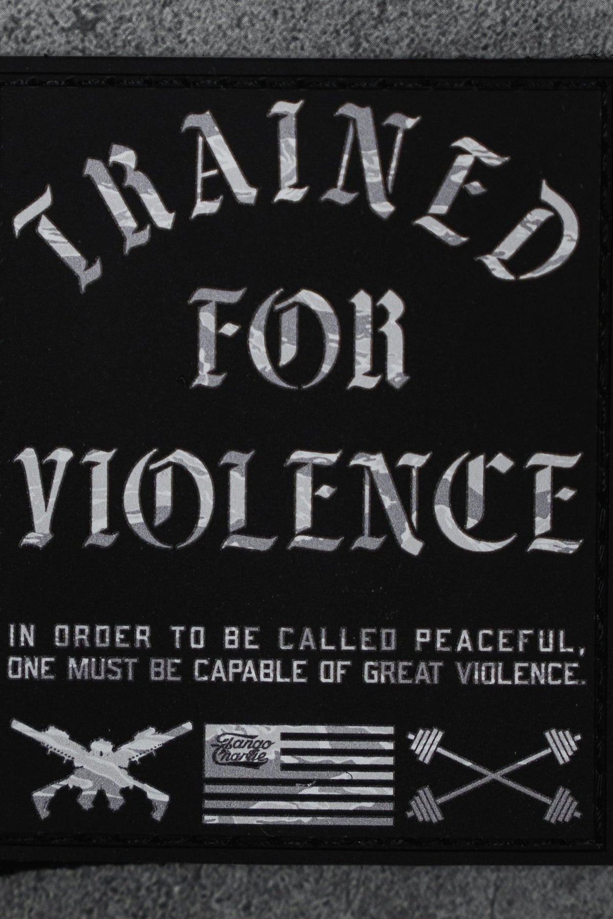 The Trained For Violence - Patch by Tango Charlie Apparel is a 3" black Velcro patch featuring bold white "TRAINED FOR VIOLENCE" text, crossed rifles, arrows, a black-and-white flag, and a striking 3D PVC design.