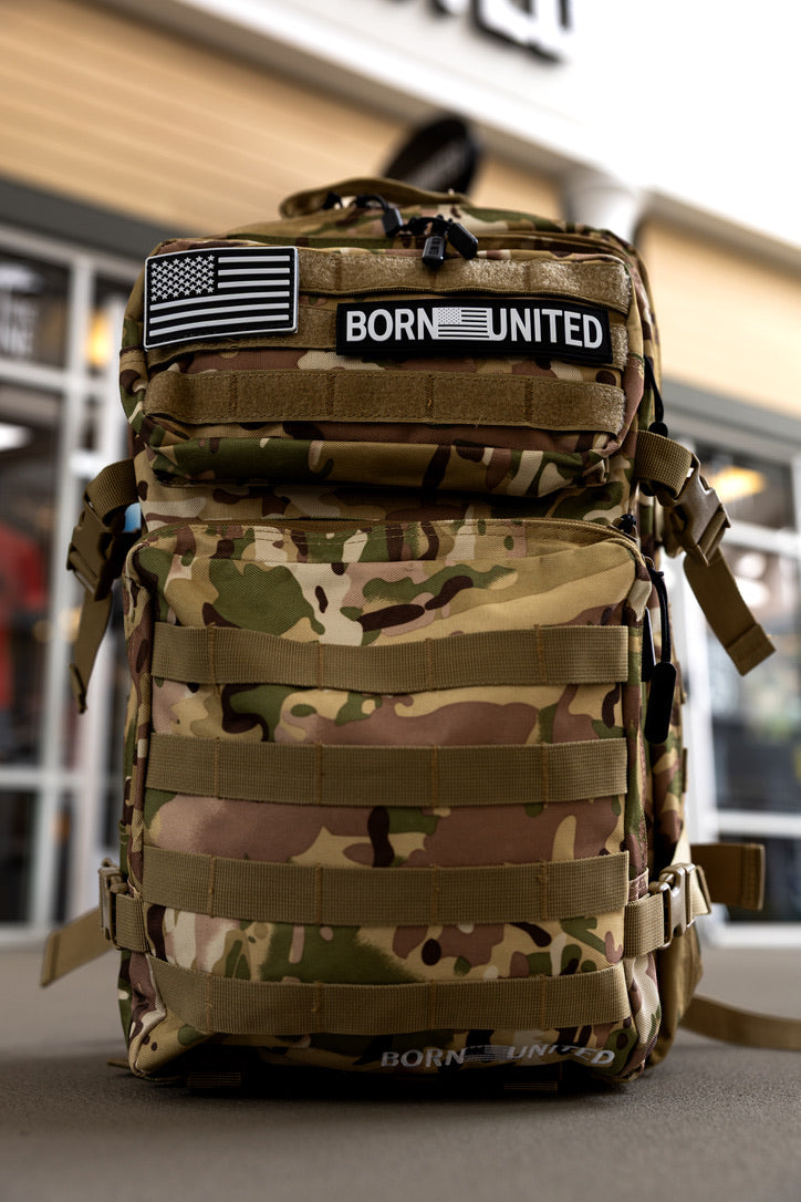 The OCP Tac-Pac - 45L by Born United Private Label, featuring BORN UNITED and American flag patches, stands upright outdoors against a building.