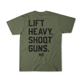 The Lift Heavy. Shoot Guns. shirt by Tango Charlie Apparel is olive green, made from soft combed ringspun cotton/polyester, and features bold black text on the back with a small American flag logo and DOMINATE underneath.