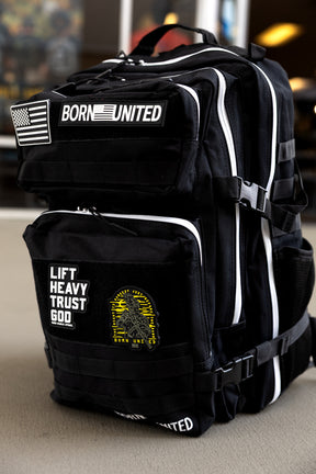 The Apex Premium Tac-Pac - 45L by Born United Private Label is a black tactical travel backpack with white zippers, featuring patches: an American flag, BORN UNITED, LIFT HEAVY TRUST GOD, and a yellow gorilla graphic. Displayed on a light surface.