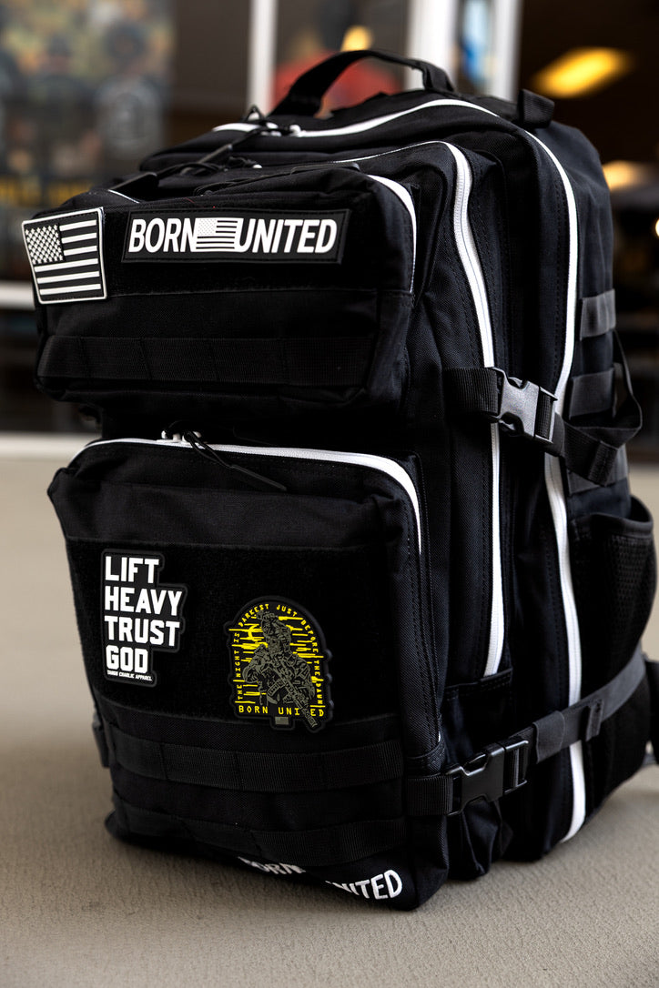 The Apex Premium Tac-Pac - 45L by Born United Private Label is a black tactical travel backpack with white zippers, featuring patches: an American flag, BORN UNITED, LIFT HEAVY TRUST GOD, and a yellow gorilla graphic. Displayed on a light surface.