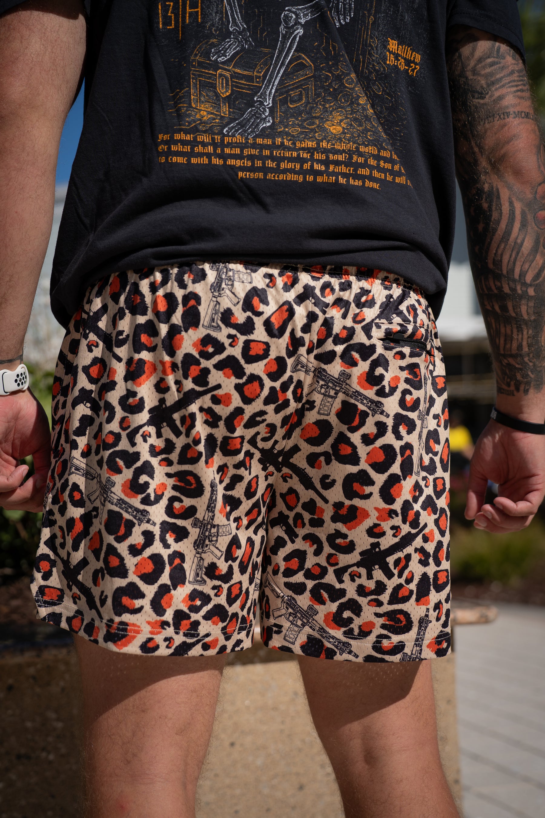A person faces away outdoors in Tango Charlie Apparel’s Men’s Mesh Lifestyle Shorts | 5.5"- Loaded Leopard, styled with a black graphic tee and white wristwatch.