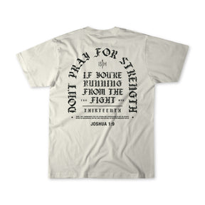Introducing the Be Strong Premium Tee by 13th—a white, high-quality shirt featuring bold black gothic-style text on the back: “Don’t pray for strength if you’re running from the fight,” referencing Joshua 1:9. This powerful statement piece is a standout addition to our faith apparel collection.