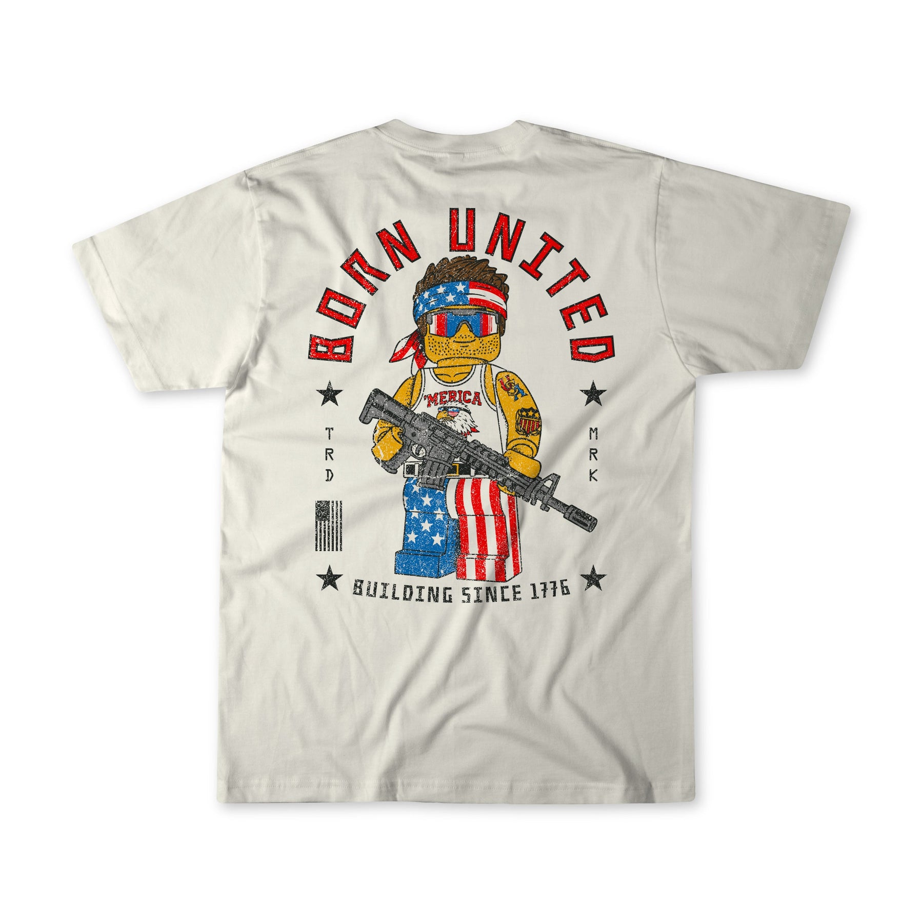 The Brick America white t-shirt by Born United Private Label showcases a muscular teddy bear in patriotic gear, wielding a rifle and shield with the US flag. "BORN UNITED" and "BUILDING SINCE 1776" text highlight its patriotic brick strength.