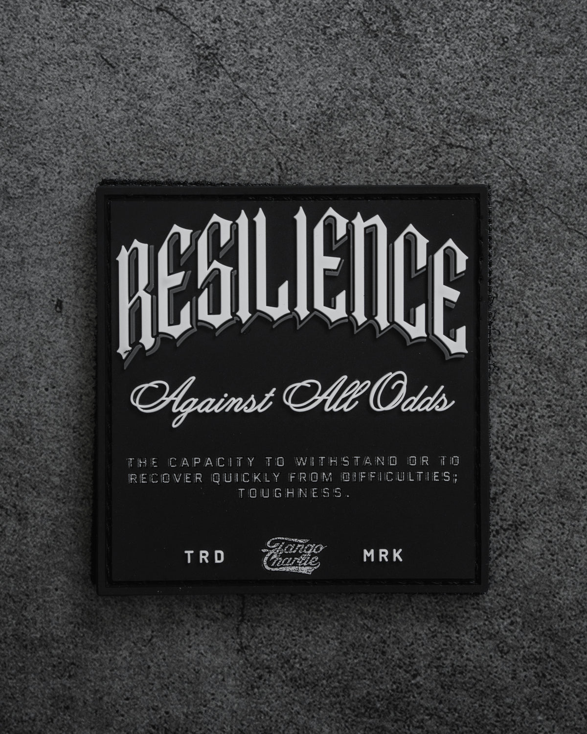 The Resilience-PVC Patch by Tango Charlie Apparel features bold RESILIENCE Against All Odds text and a definition on a black patch with a gray background, symbolizing toughness and the capacity to recover from difficulties.