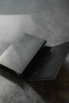 On a textured dark surface, the sleek black Relentless Betrayal Minimalist Wallet is open. Its smooth metallic exterior contrasts with the soft dark interior, and light reflects off its pop-up design and RFID blocking credit card protection features.