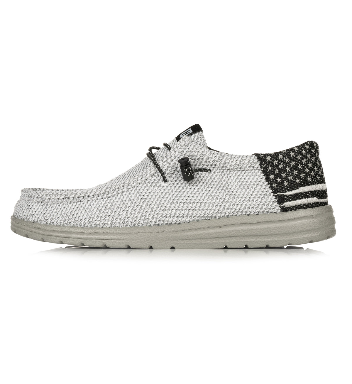 The Howitzer Clothing Roam Blackout - Gray is a casual, light gray slip-on shoe with laces, a black heel detailed with white stars and stripes, and a textured sole.