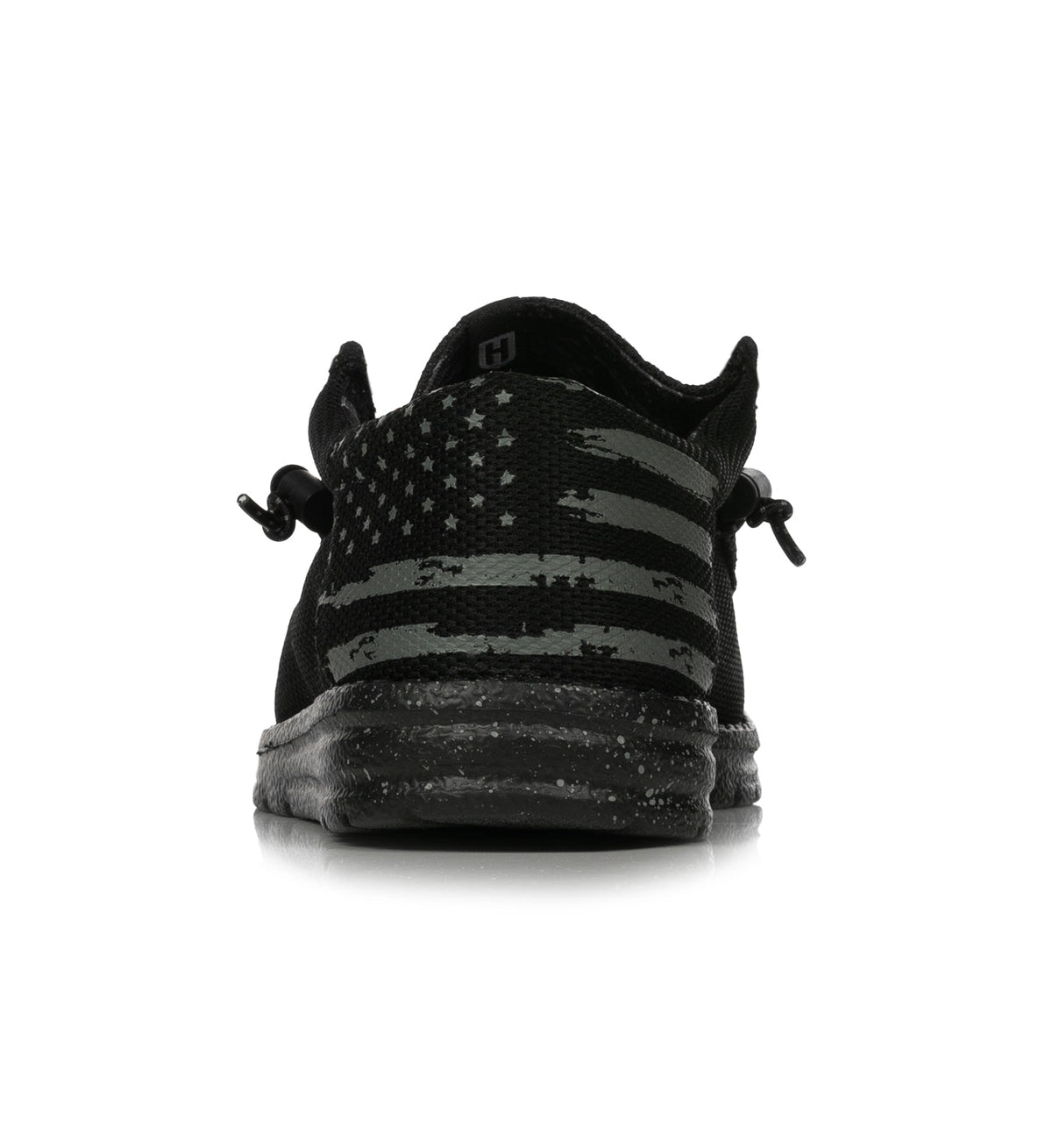 The Howitzer Clothing Roam Blackout is a black athletic shoe shown from the back, featuring a stylized gray American flag on the heel and a speckled sole, set against a white background.
