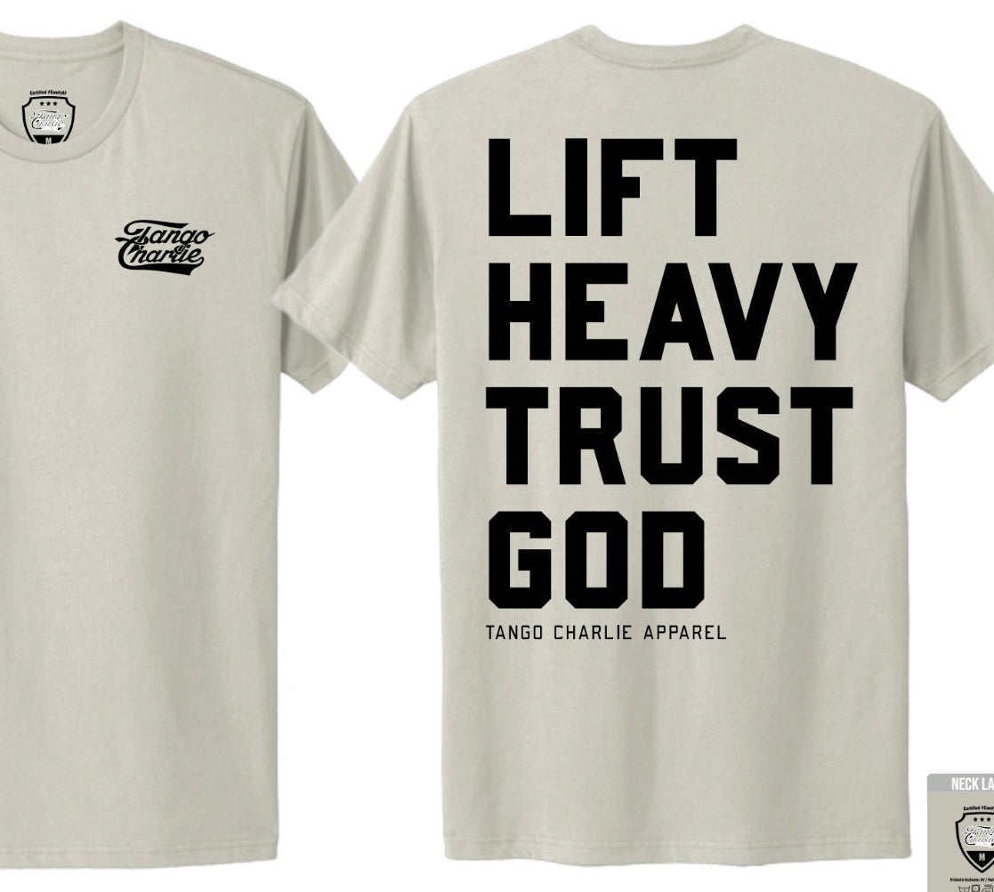 The Lift Heavy. Trust God. - Tee by Tango Charlie Apparel features a beige color, front left chest logo, and bold black "Lift Heavy Trust God" text with the brand below on the back, inspired by Christian fitness and Proverbs 3:5-6.