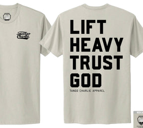 The Lift Heavy. Trust God. - Tee by Tango Charlie Apparel features a beige color, front left chest logo, and bold black "Lift Heavy Trust God" text with the brand below on the back, inspired by Christian fitness and Proverbs 3:5-6.