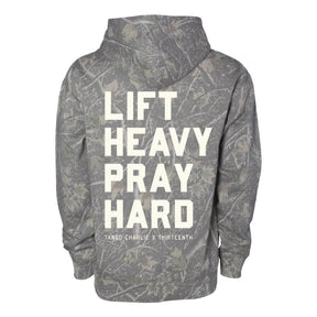 The Lift Heavy. Pray Hard. - Deadwood Camo Hoodie by Tango Charlie Apparel features bold white lettering to inspire spiritual strength in and out of the gym.