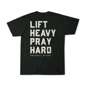 The Lift Heavy. Pray Hard. - Black Tee by Tango Charlie Apparel features bold white “LIFT HEAVY PRAY HARD” text on the back and “TANGO CHARLIE X THIRTEENTH” below, symbolizing resilience.