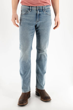 A person is wearing Devil Dog Dungarees Boot Cut Jean - Williamston in light blue, paired with a pink t-shirt and brown leather boots, standing against a plain white background. The photo is cropped from the shoulders down.