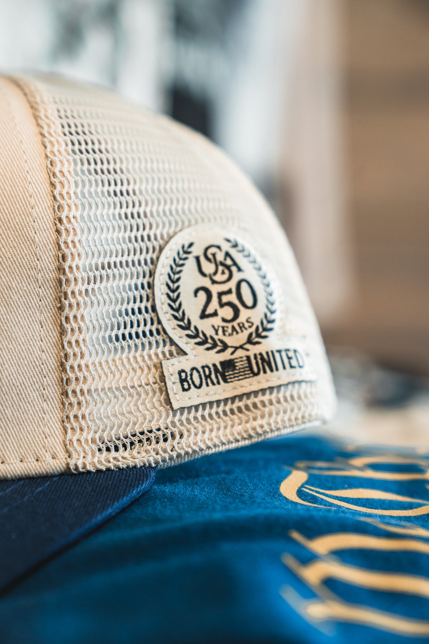 Close-up of the ’Merica Trucker Snapback by Born United Private Label, featuring a breathable mesh design and a patch that reads “USA 250 Years Born United,” accented by a laurel wreath. This classic snapback blends comfort with style, making it the ideal modern handmade hat for celebrating history.