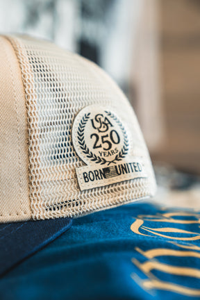 Close-up of the ’Merica Trucker Snapback by Born United Private Label, featuring a breathable mesh design and a patch that reads “USA 250 Years Born United,” accented by a laurel wreath. This classic snapback blends comfort with style, making it the ideal modern handmade hat for celebrating history.