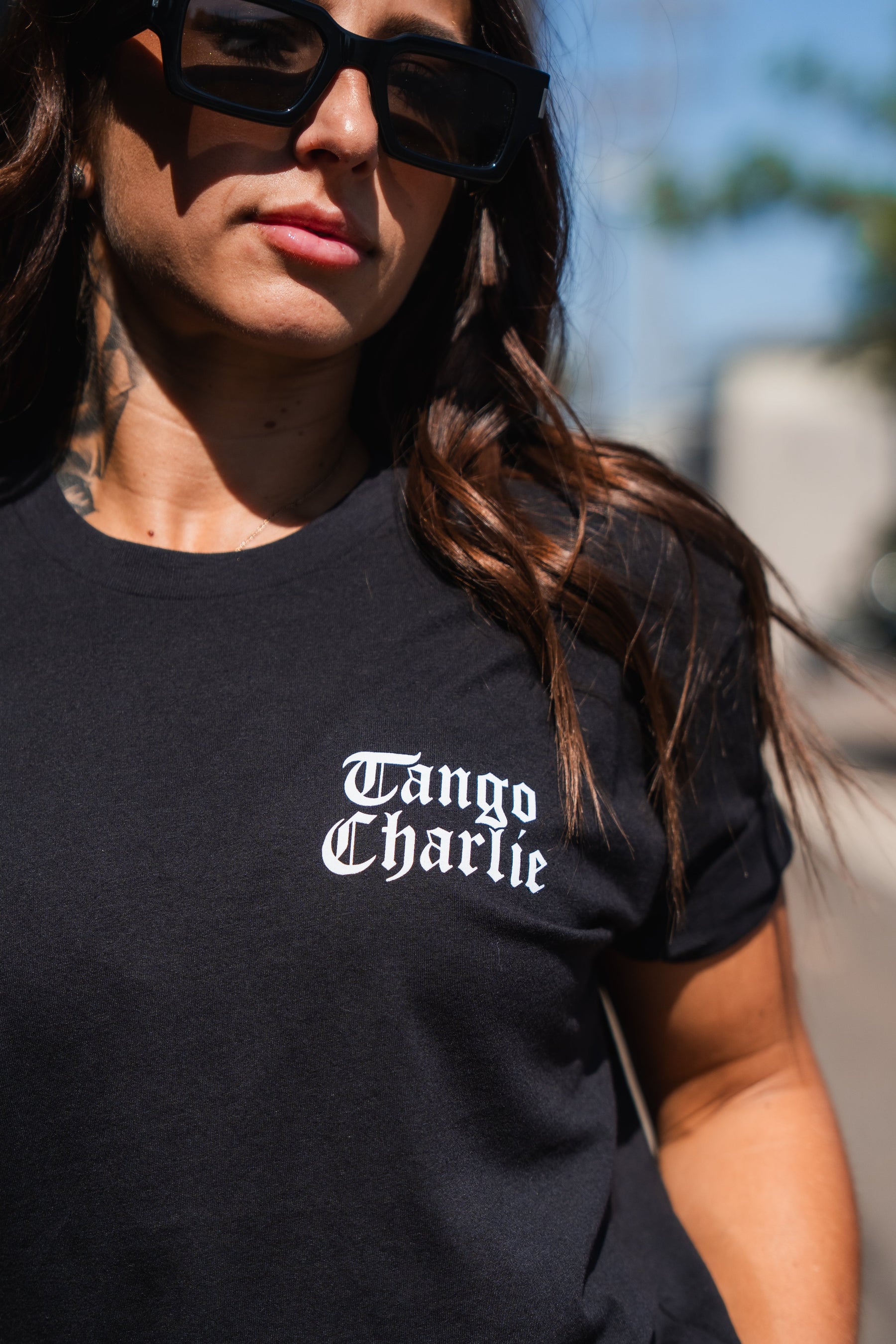 A woman wearing a black Lift Heavy. Praise Hard. Black Tee with Tango Charlie printed in white gothic lettering on the chest.