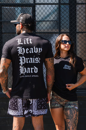 A man wearing a black Lift Heavy. Praise Hard. Black Tee and a woman wearing a black t-shirt with an Isaiah 41:10 logo on the front.