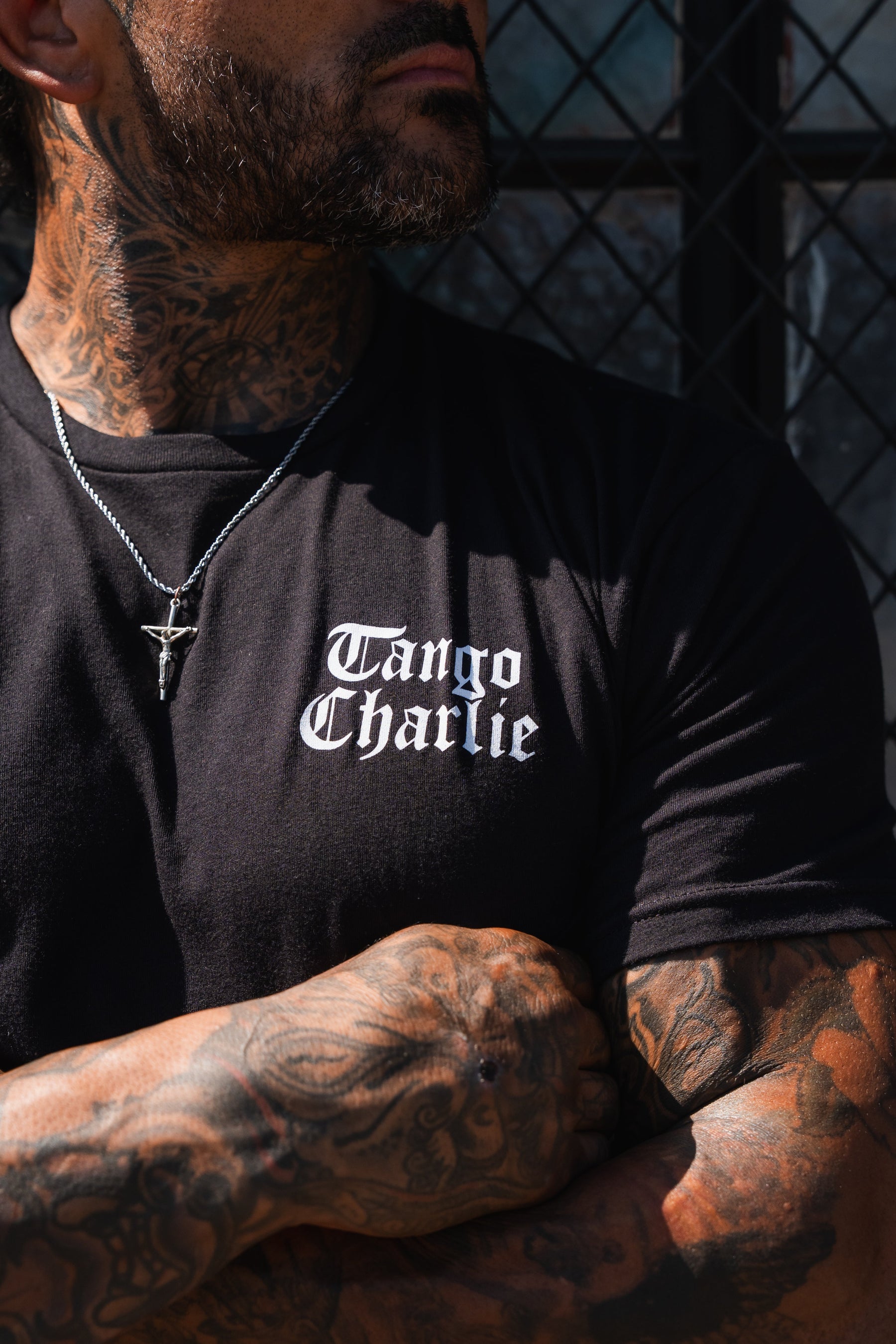 A man with tattooed arms and neck wears a black Lift Heavy. Praise Hard. Black Tee by Tango Charlie Apparel.