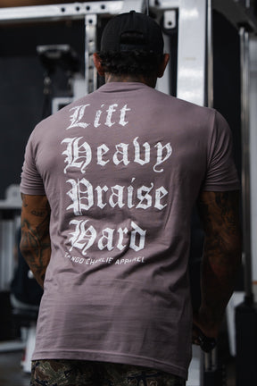 Person wearing a mauve Lift Heavy. Praise Hard. Shiitake Tee with Lift Heavy, Praise Hard printed on the back in a white gothic-style font.