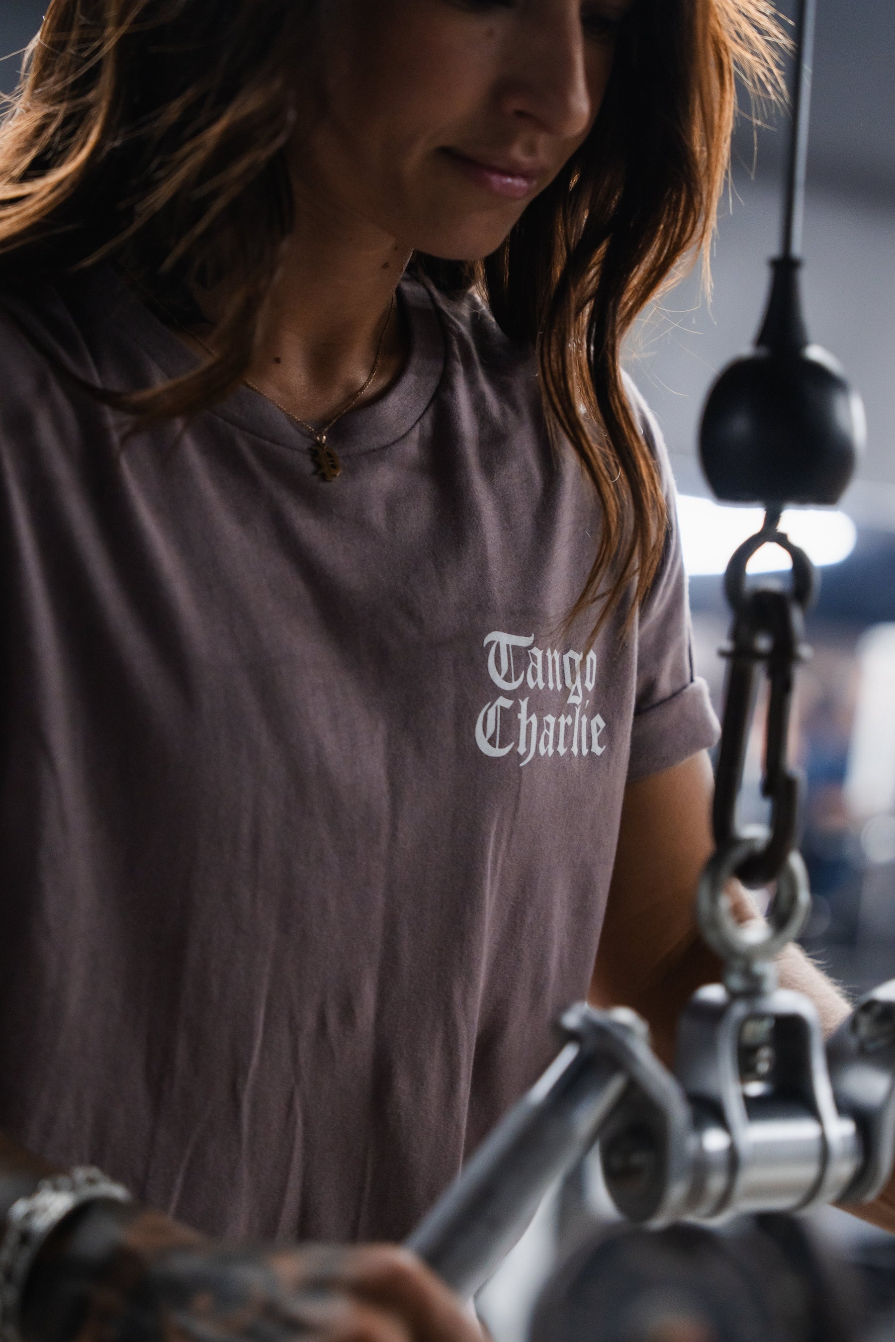 A person wearing a grey Lift Heavy. Praise Hard. Shiitake Tee with Isaiah 41:10 in white gothic lettering performs a cable exercise at the gym.