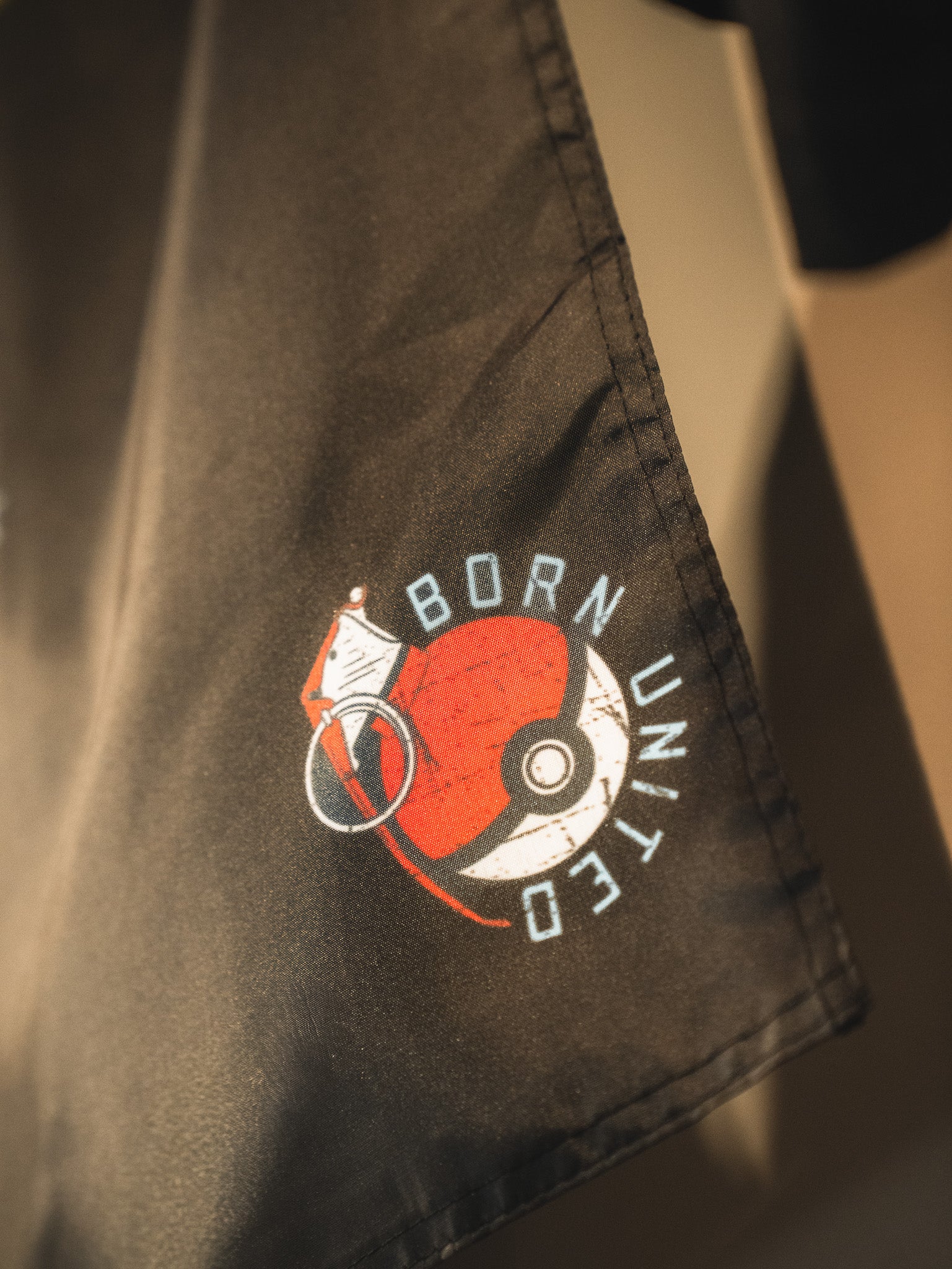 A close-up of dark fabric features the Pika-Pew Flag from Born United Private Label—a collector's must-have for tactical Pokémon fans, showcasing a Poké Ball graphic, "BORN UNITED" text, and a white flag design.