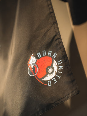 A close-up of dark fabric features the Pika-Pew Flag from Born United Private Label—a collector's must-have for tactical Pokémon fans, showcasing a Poké Ball graphic, "BORN UNITED" text, and a white flag design.