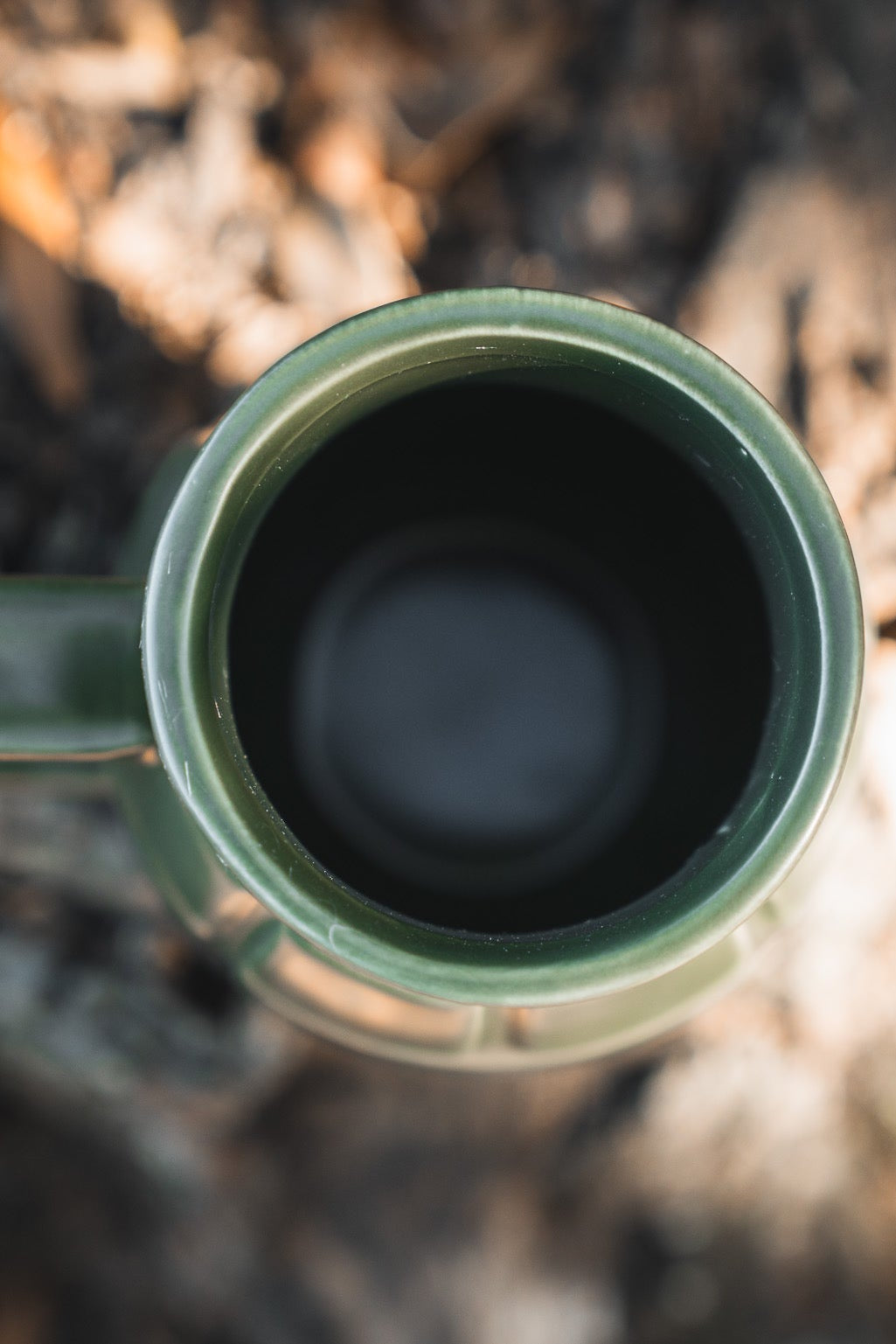 Close-up, top-down view of the BU Sip Sip Boom Mug by Born United Private Label, hand-crafted with a handle and placed on a blurred outdoor surface, possibly soil or wood.
